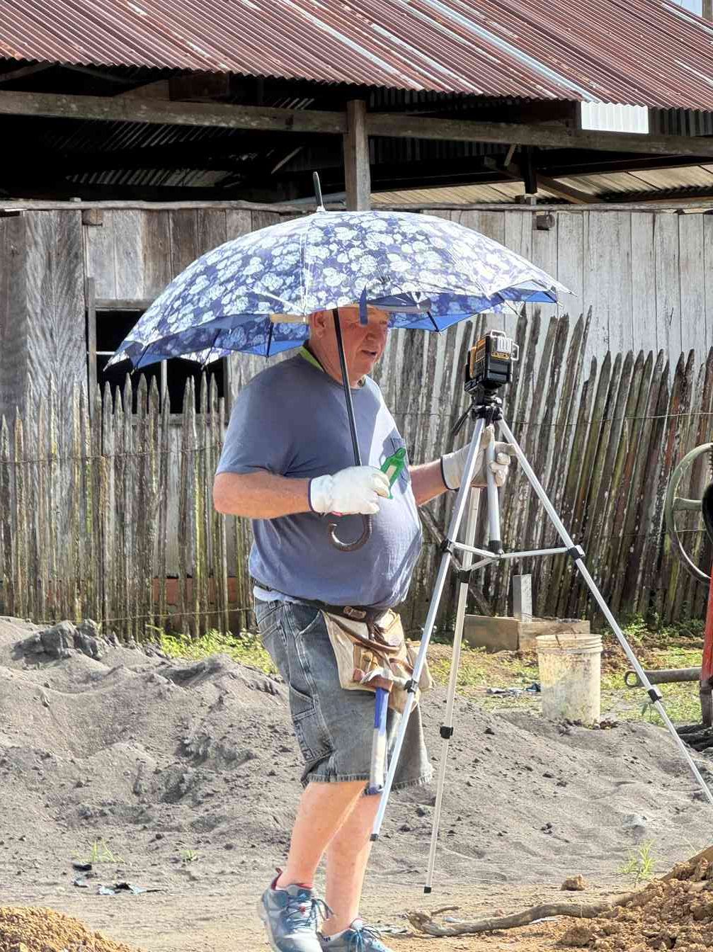 A team member setting up a surveying level, sheltering under an umbrella
