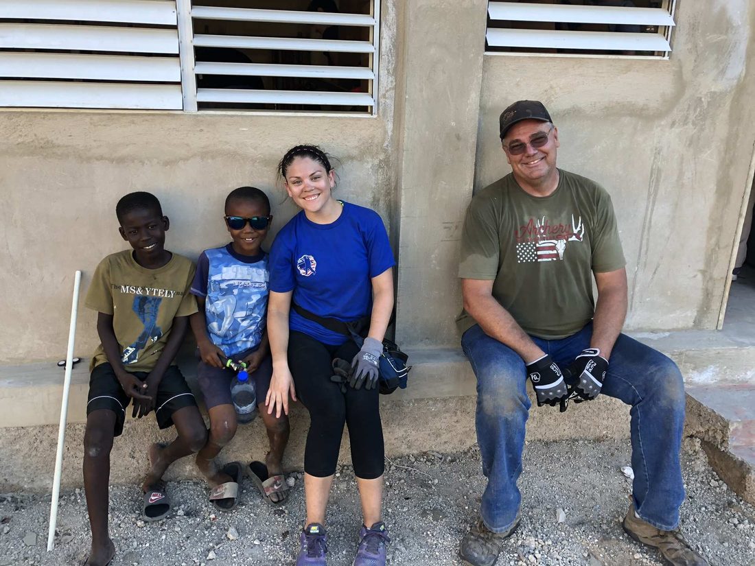 Two team members sitting with children outside a newly built home